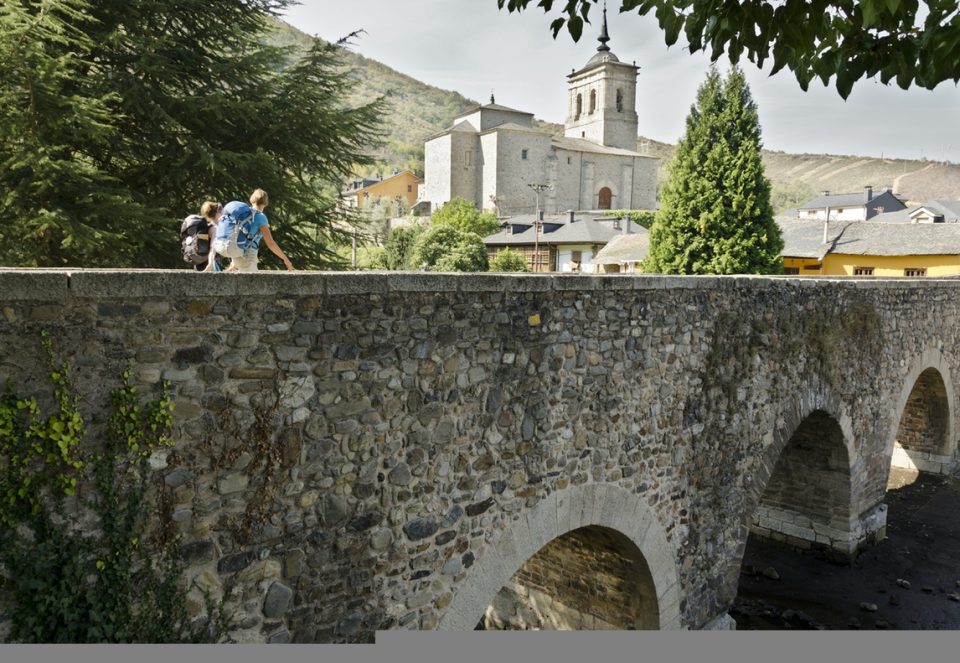 Two female Camino pilgrims crossing a medieval bridge in Leon (Spain) on their way to Santiago de Compostela.