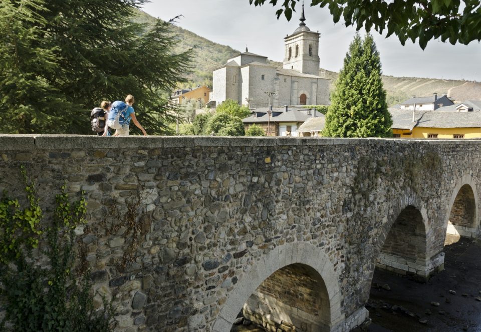 Two pilgrims on their way to Santiago de Compostela cross a medieval bridge over the river Meruelo in Molinaseca (León).