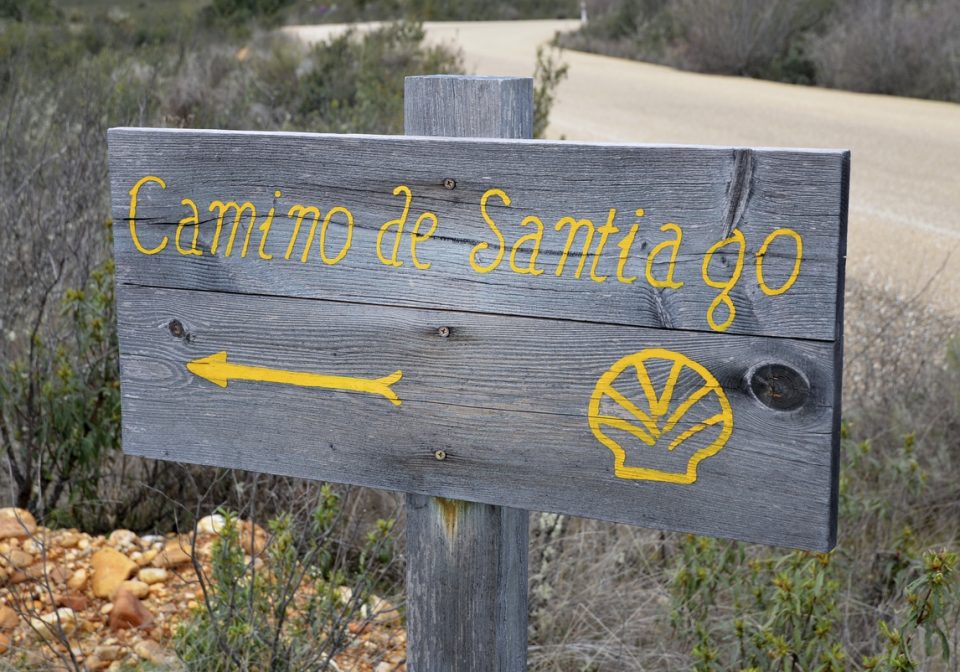 Wooden sign saying Camino de Santiago and the iconic shell in yellow