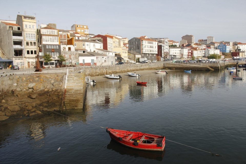 red rowing boat on the water with harbour in the background
