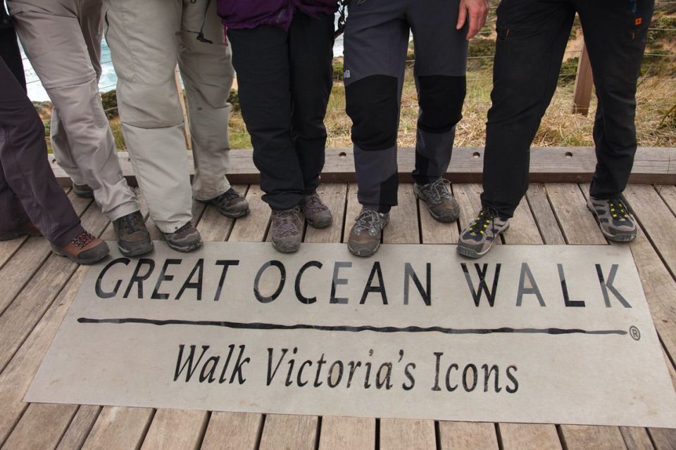 Several pairs of hiking boots partially covering the Great Ocean Walk sign on a boardwalk