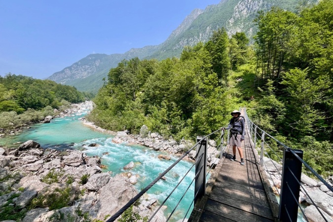 Hiker standing on a bridge over the turquoise Soca River in Slovenia