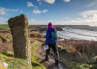 Hiker South West Coast Path Female hiker in a pink beanie walks along the South West Coast Path along a muddy trail under a blue sky