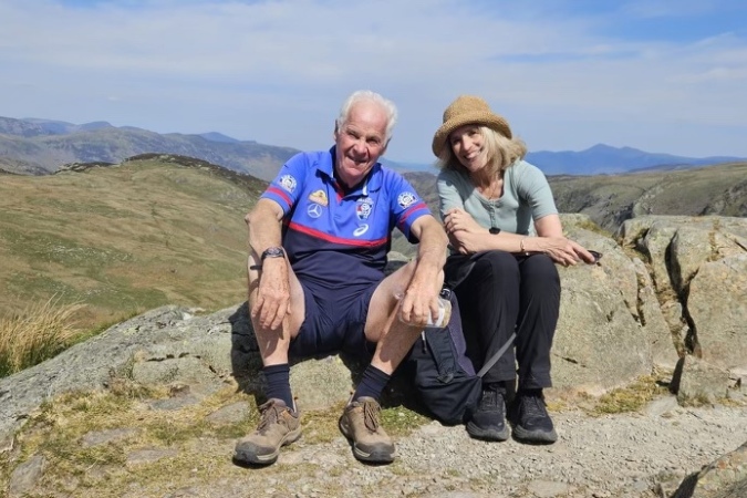 Two hikers resting on a boulder and smiling at the camera in the Lake District National Park in England