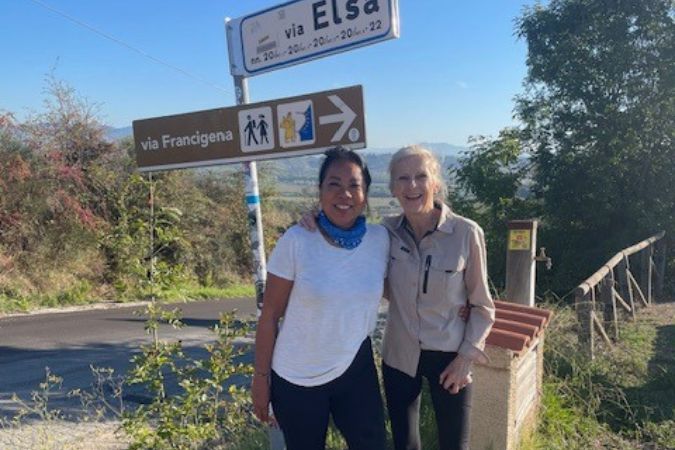 Two female hikers standing next to a waymarker for Italy's Via Francigena pilgrim trail