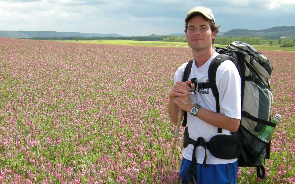 Hiker walking with flowers behind.