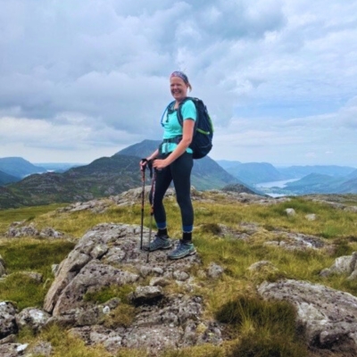 Female hiker in blue t-shirt on England's Coat to Coast Path. She is smiling at the camera and there are hills in the background.