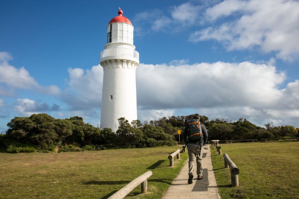 Male hiker walking along a path towards a white lighthouse