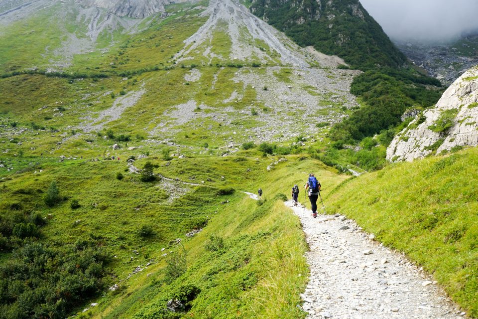 Hikers along the path surrounded by very green slopes in mountains.