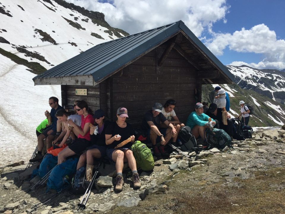 Hikers sitting around hut on mountain side sheltering from hot sun.