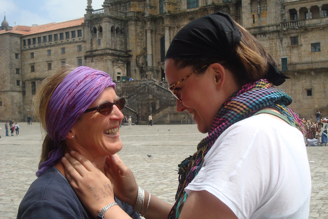 Closeup of two women smiling at each other in front of the Santiago Cathedral after walking the Camino Frances through Spain.