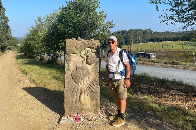 Walker on the Camino de Santiago in Spain standing next to a stone marker with a scallop shell