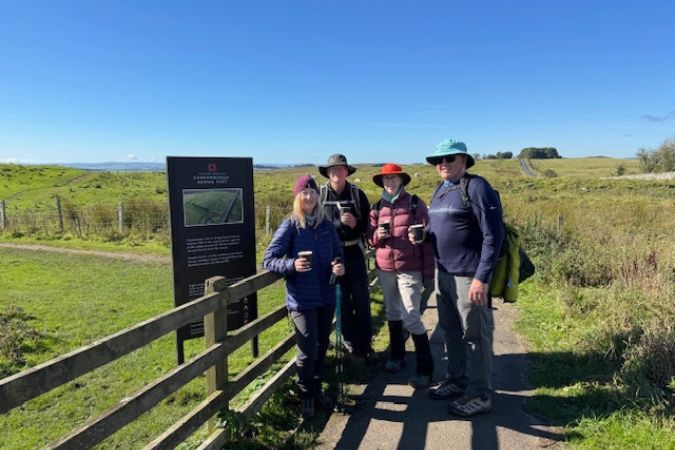 Hikers enjoying a sunny day on Hadrian’s Wall Path, smiling for a group photo with coffee in hand.