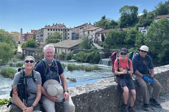 Pilgrims on Spain's Camino de Santiago resting on a stone bridge.