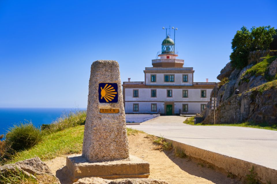 The famous Cape Finisterre lighthouse in Galicia behind a stone marker for the Camino showing 'zero' km.