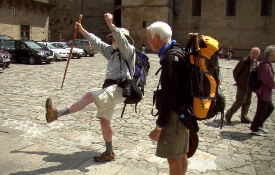 Two male pilgrims in the main square of Santiago, one with arms raised in celebration of completing their Camino pilgrimage