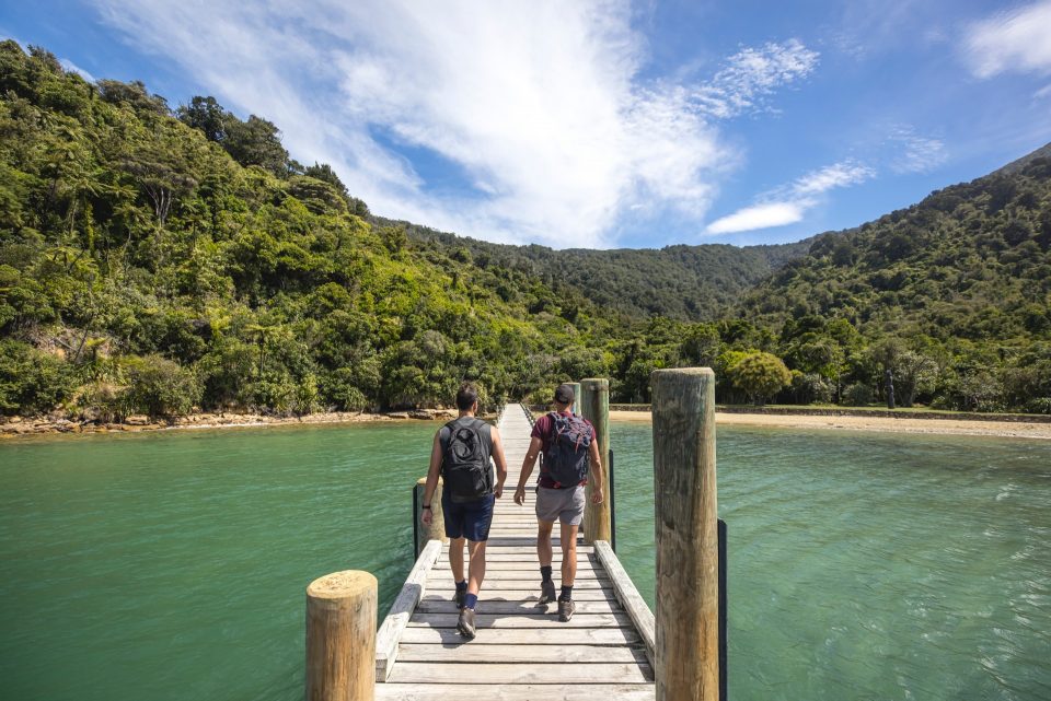 Two hikers walking along a jetty to start their walk on the Queen Charlotte Track