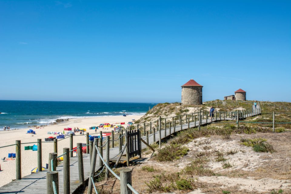 Wooden boardwalk and a beach with colourful beach shelters and tourists, on the Portuguese Coastal Camino.