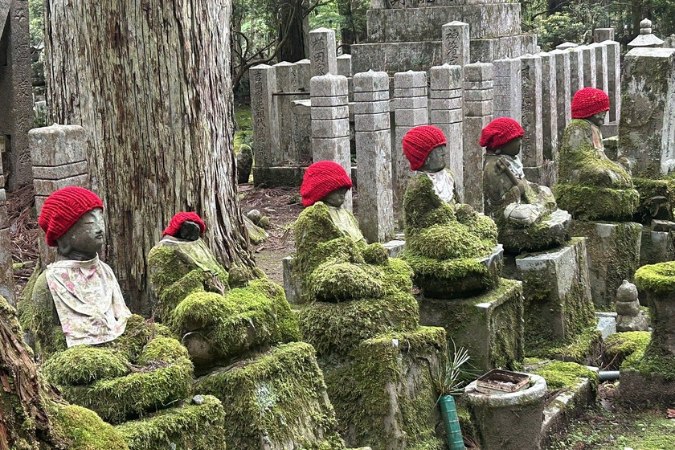 Small moss-covered stone statues shaped like children and adorned with red hats, along the Kumano Kodo trail in Japan.
