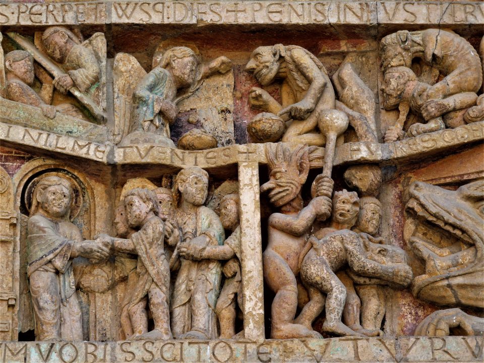Decorative stone wall carving on the Sainte Foy abbey church in Conques on Le Puy Camino showing a closeup of tortures and punishment from the Last Judgment.