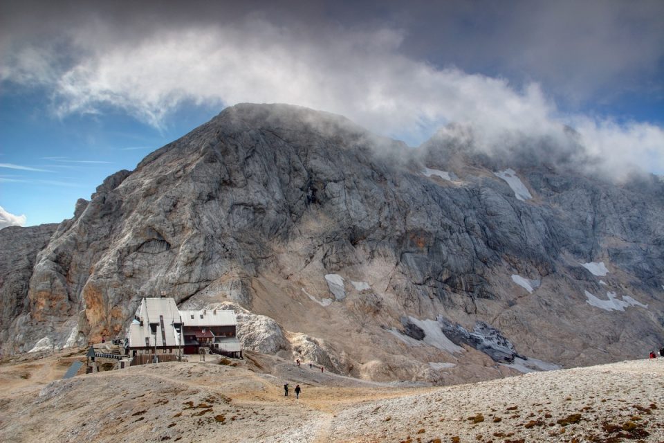 KRANJSKA GORA 2018: Hikers walk on barren Kredarica plateau near Triglavski dom na Kredarici mountain hut in Julian Alps with cloud covered Triglav the highest Slovenian peak