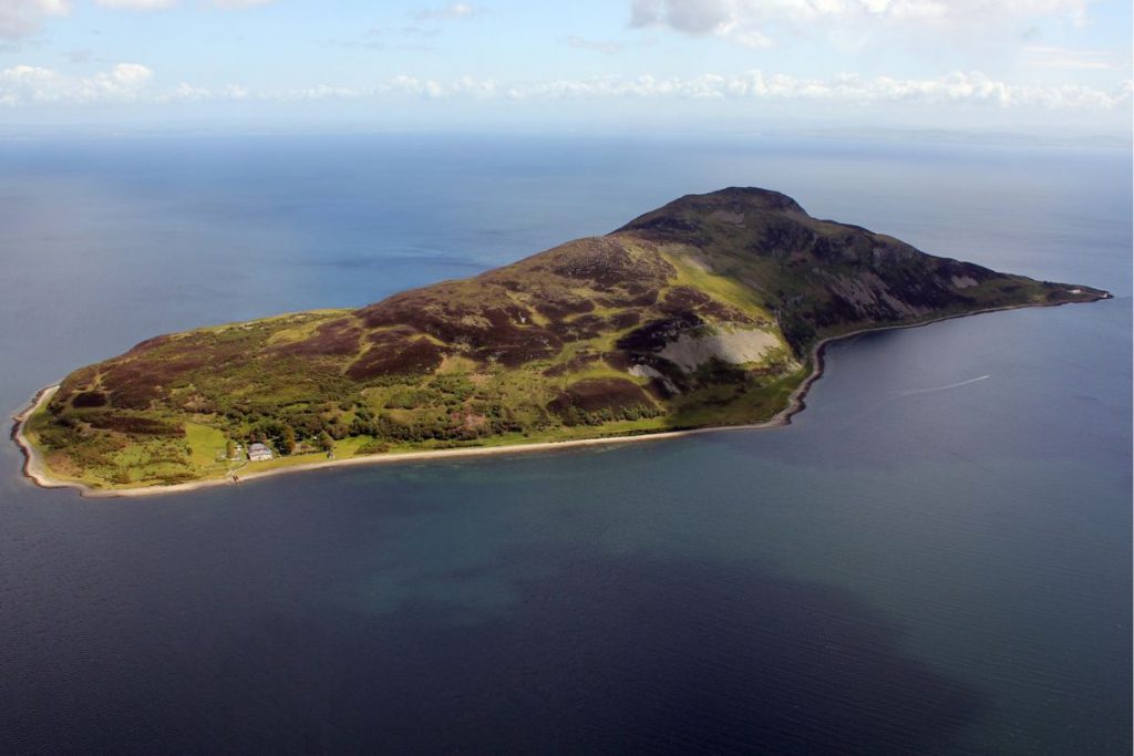 Aerial view of a small and green Holy Isle surrounded by the dark sea.