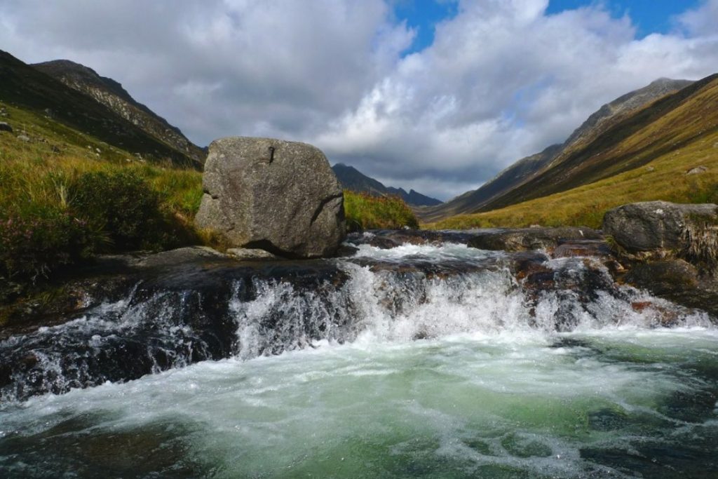 Rushing water in a rock pool known as Glen Rosa with mountains in the background.
