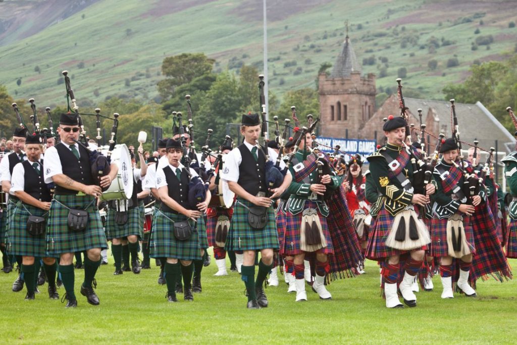 Massed Pipe Bands performing together outside on a green lawn a the Brodick Highland Games.