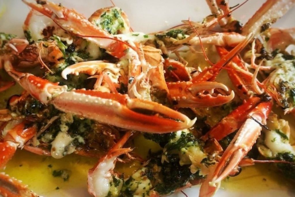 Closeup of a plate of bright orange crab claws with herb sauce.