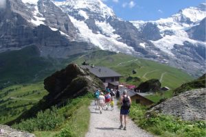 Group of hikers ascending trail to rustic mountain cabin.