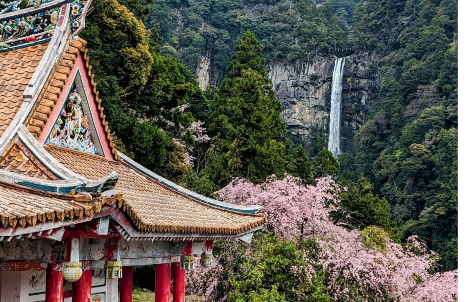 A serene Japanese temple surrounded by pink cherry blossom and a cascading waterfall in the background