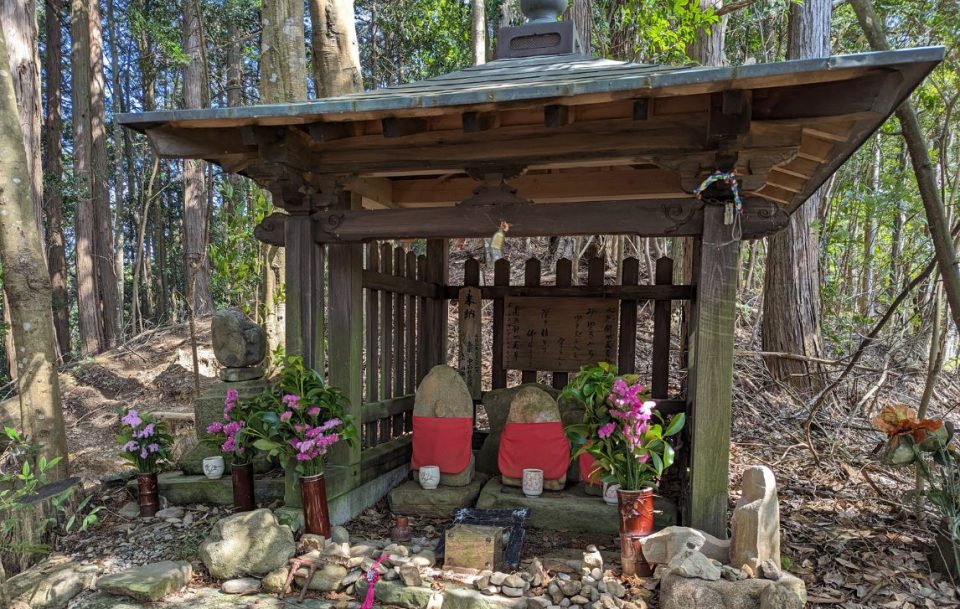 Japanese shrine in the forest with vases of bright pink flowers and stone statues