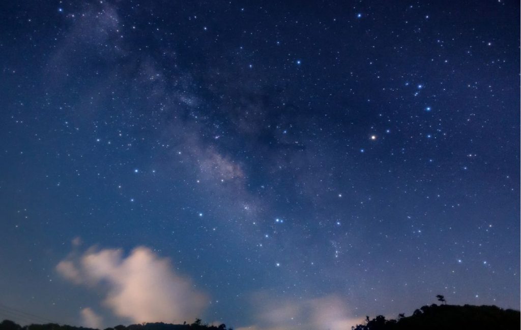 Stars illuminated in the night sky above mountains.