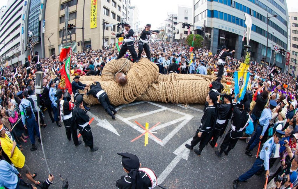 Image of a lively parade with a massive group of participants pulling a giant rope, symbolising teamwork and camaraderie.