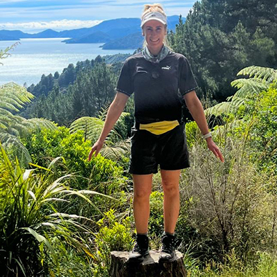 Tamara Loschiavo RAW Travel staff member Tamara on a lush green forest trail with New Zealand's Marlborough Sounds in the background.
