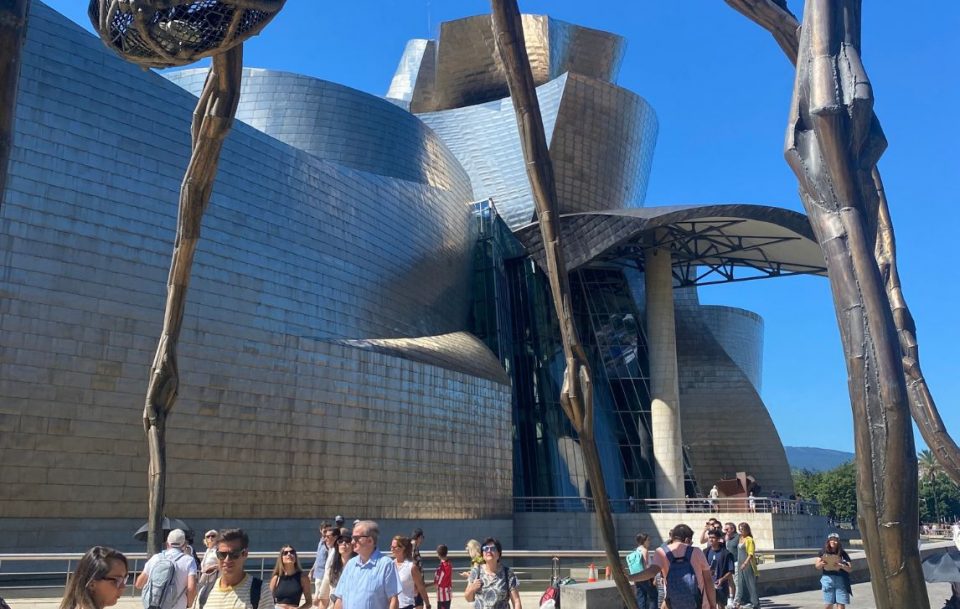 Visitors walk along the exterior of the Guggenheim Museum in Bilbao in Northern Spain highlighting its iconic structure and the lively surroundings.