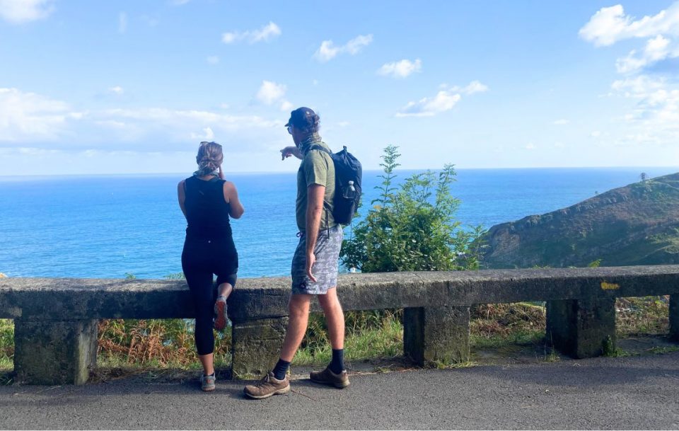 Two hikers standing side by side, observing the expansive ocean view along the Camino del Norte pilgrim trail in Northern Spain.