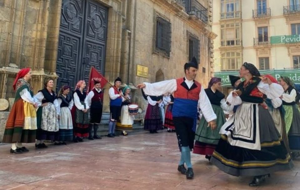 A gathering of dancers in cultural costumes celebrating with a performance in front of a prominent building in Northern Spain.