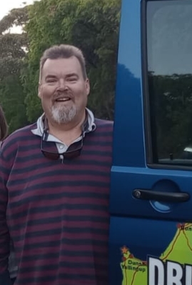 A man in a striped top stands next to the blue door of his vehicle which he uses to transport clients along the Cape to Cape Track in Western Australia