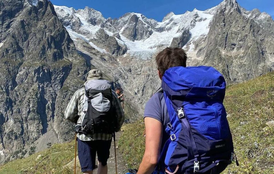 hikers walking up the Tour du Mont Blanc. You can see them from behind. They have their day packs on their backs.