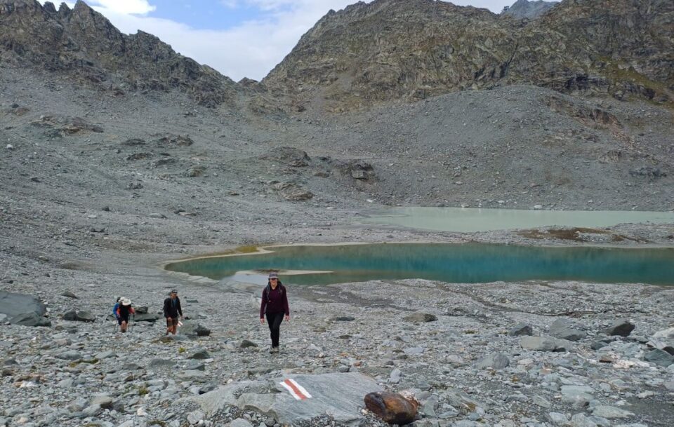 Hikers navigating their way across a rocky barren boulder field on the Walker's Haute Route in Switzerland.