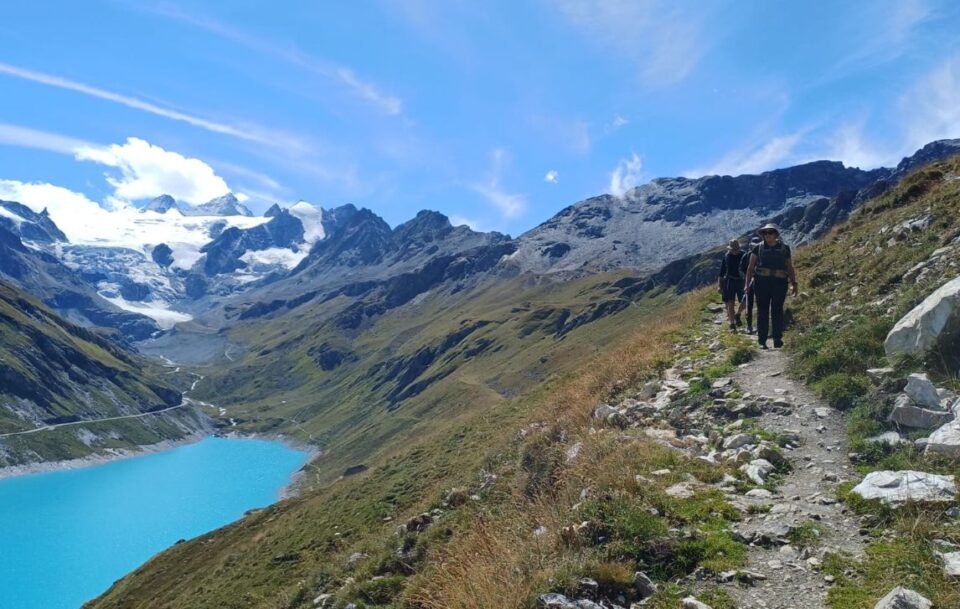 Stunning blue lake surrounded by the Alps with hikers passing on a high track.