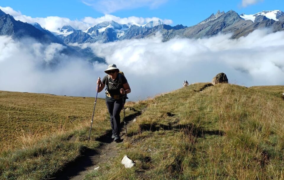 Hiker walking on the trail with clouds filling the valley and Alpine peaks emerging in the distance, Walker's Haute Route, Switzerland.