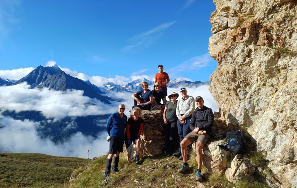 Group of happy hikers posing above the clouds with mountain peaks in the background on the Walker’s Haute Route, Switzerland.