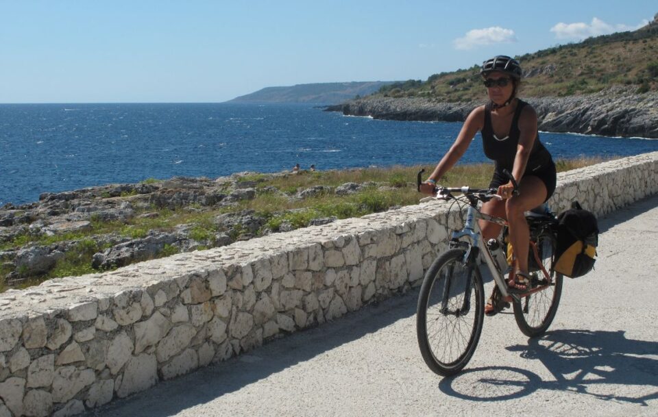 female cyclist riding along gorgeous blue ocean coast in Puglia