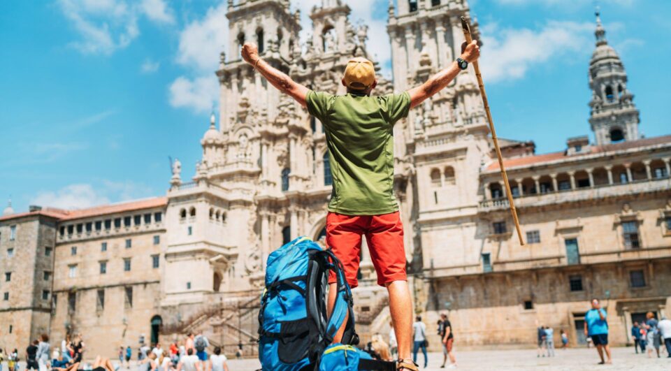 Hiker with his arms in the air displaying accomplishment after finishing the Camino hike in front of the cathedral in Santiago - Spain.