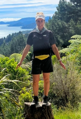 Tamara standing on a tree stump with lush green scenery behind her.