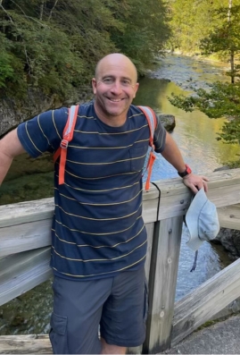 Troy leaning against a fence with gorgeous river behind him enjoying nature