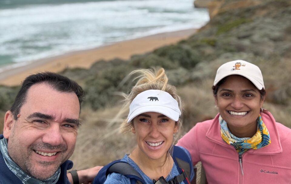 Closeup of three hikers on the Great Ocean Walk, with the beach and ocean blurred in the background.