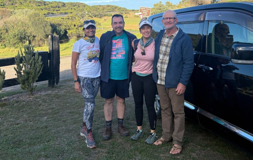 Four smiling hikers standing next to a private transfer vehicle on the Great Ocean Walk near Castle Cove Lookout.